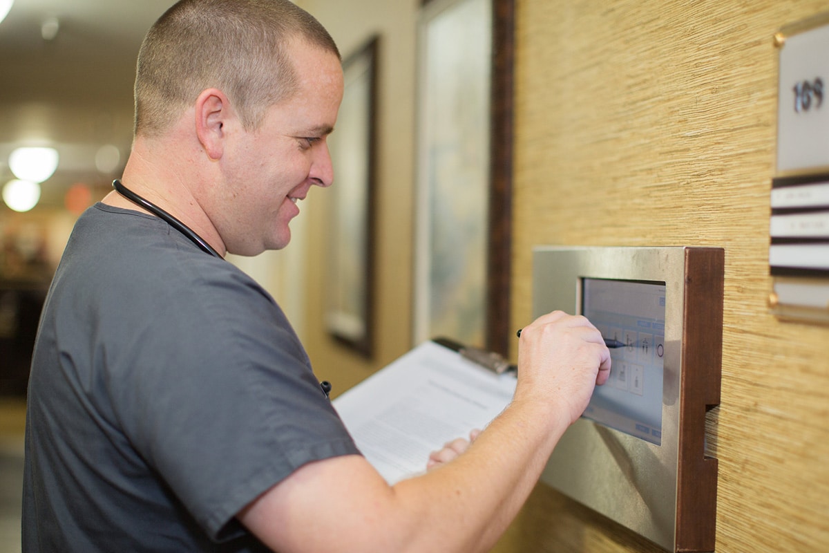 Medical professional entering information on a wall screen outside a patient room.