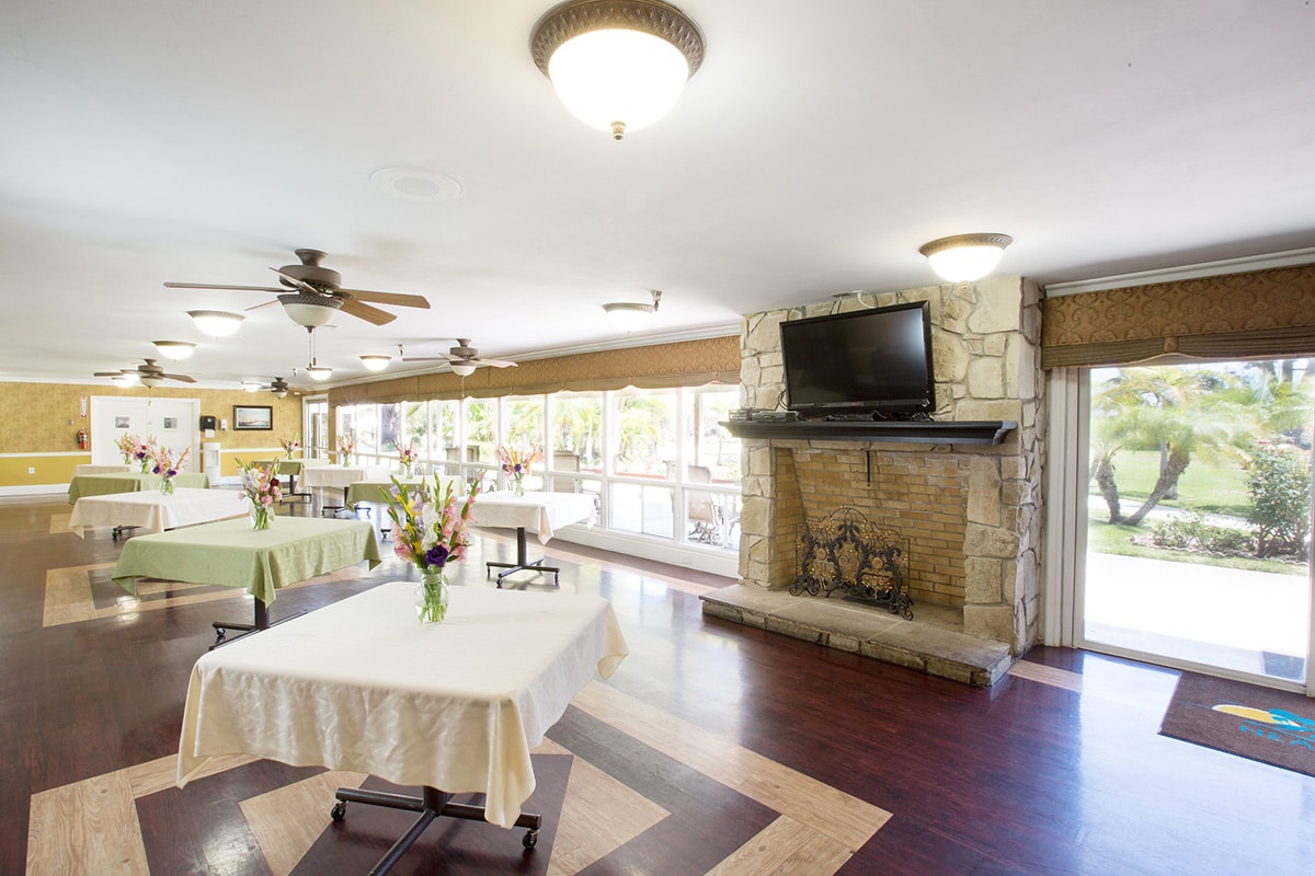 Dining room with fireplace, flat screen TV and tables with table cloths and flower arrangements on each table.