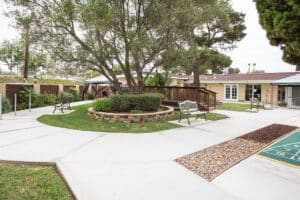 Outdoor courtyard with shuffle board, trees, walkway bridge, and benches.