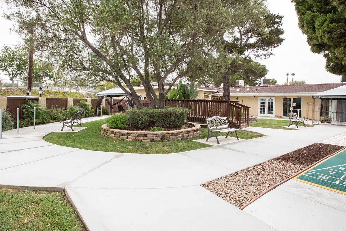 Outdoor courtyard with shuffle board, trees, walkway bridge, and benches.