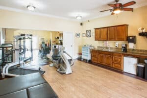 Rehab gym with machines, tables, and kitchen counter.