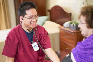 Medical professional in red scrubs taking the blood pressure of a woman in purple shirt.