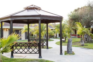 Outdoor black gazebo in the courtyard with sidewalk next to it and palm trees