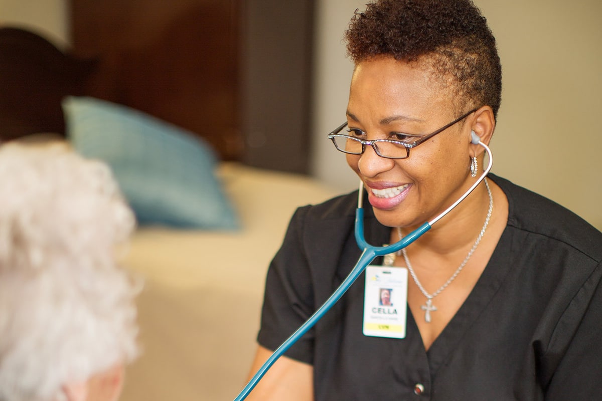 Medical professional smiling with black scrubs using a stethoscope on gray haired woman