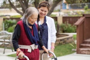 Medical professional helping woman using a walker outside.