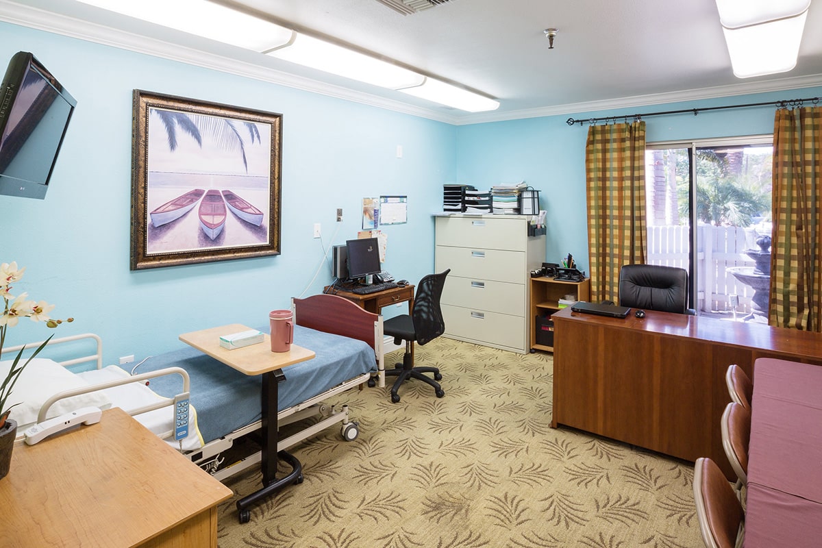 Room with desk, computer, hospital bed and flat screen tv with a view of the fountain out the sliding glass door.