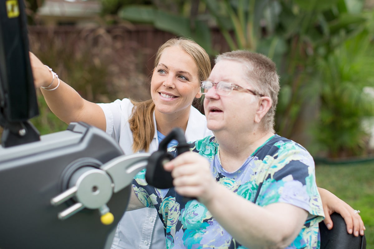 Man using rehab machine with medical professional in white jacket next to him helping him.