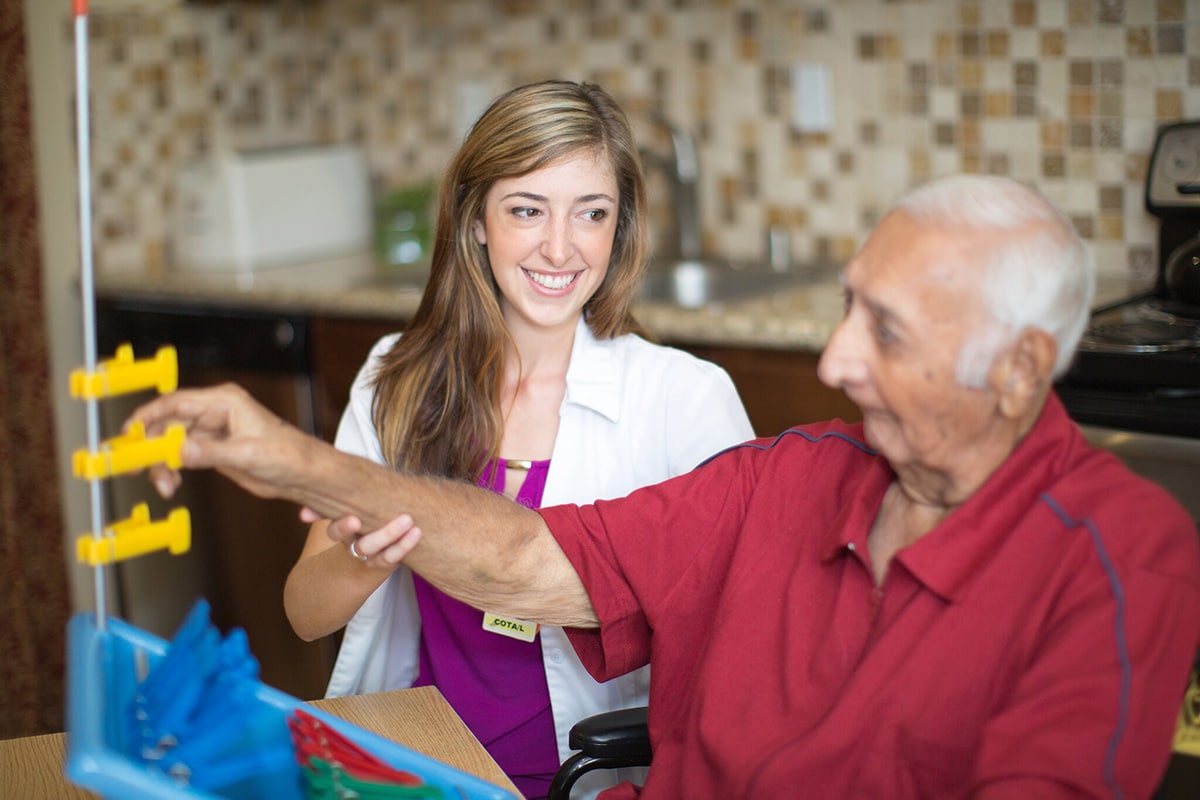 Man in red shirt working on an occupational rehab tool with medical professional in white shirt helping him.
